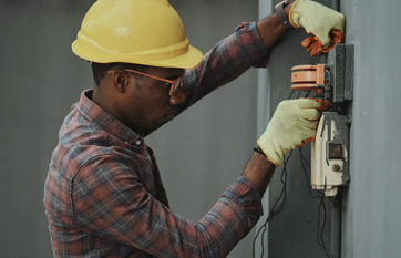 A man in yellow hard hat and gloves working on electrical box.